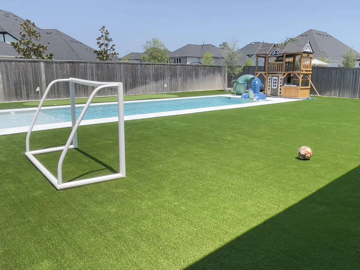 Artificial turf backyard with a pool, soccer goals and play set