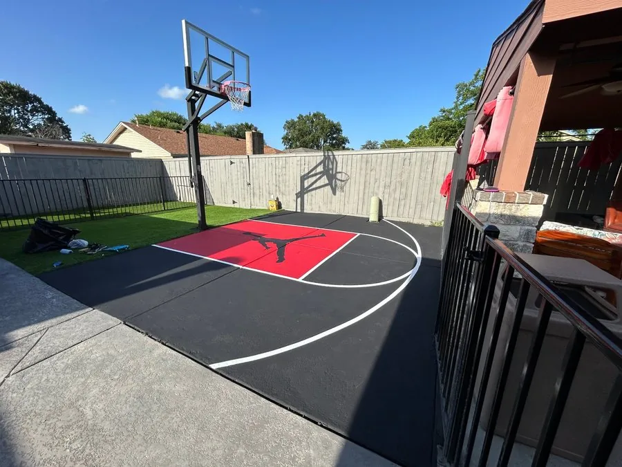 Black and red backyard basketball court with white lines, custom logo, hoop and fencing