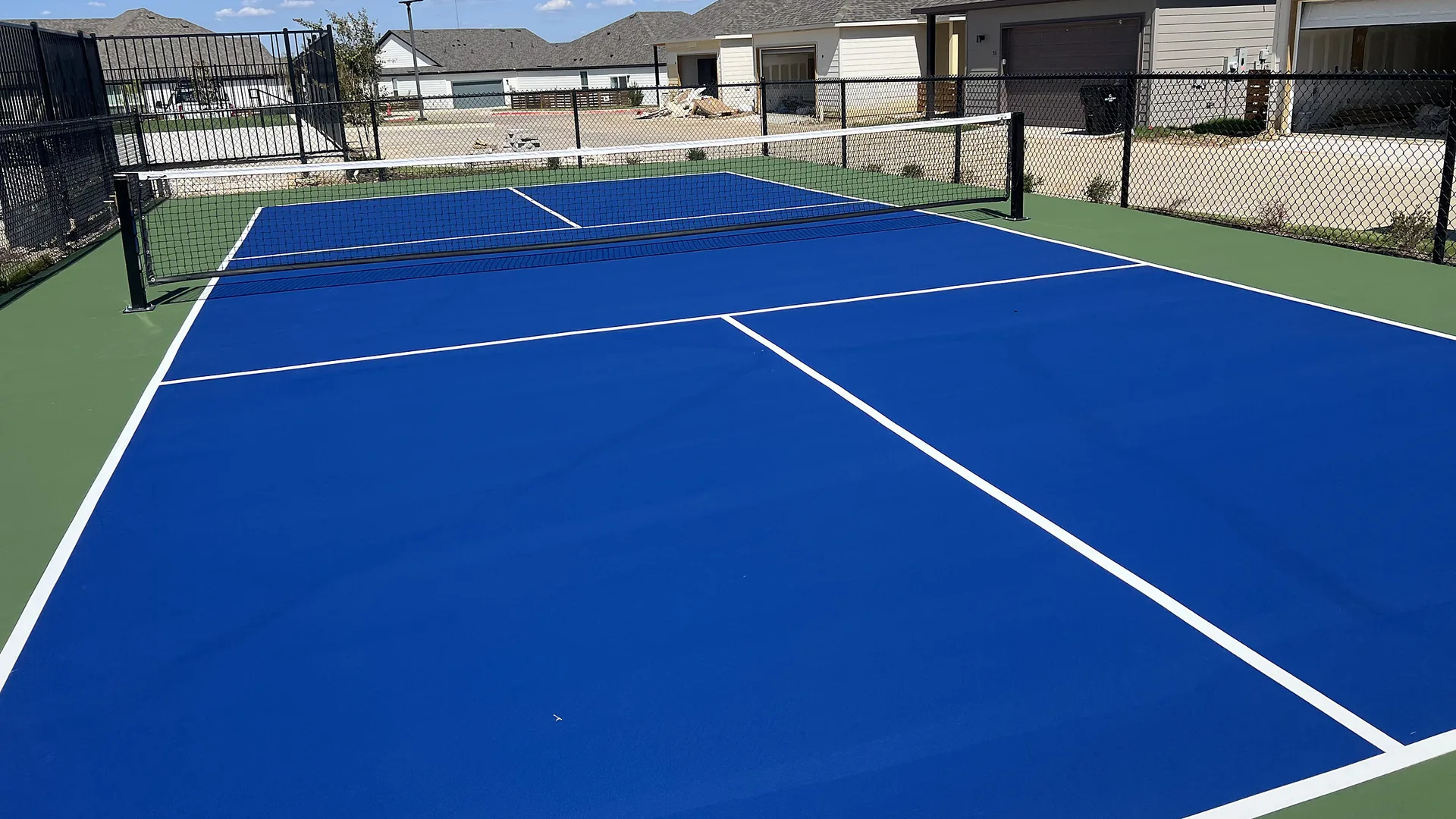 Blue backyard pickleball court with net and fencing installed by Houston Turf Specialists