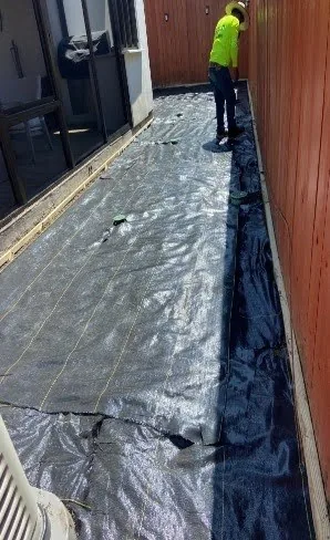Crew member laying black permeable weed barrier fabric over the yard