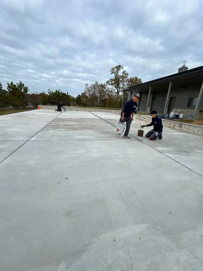 Crew members applying crack filler and patching joints on a large concrete court slab