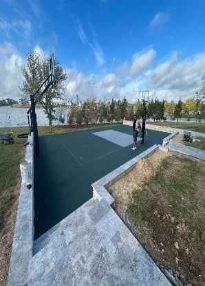 Finished dark green sport court with stone steps and two basketball hoops by a lake